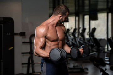 Fototapeta na wymiar Man In The Gym Exercising Biceps With Dumbbells
