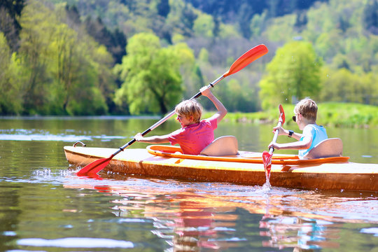 Back view of two boys kayaking on the river. Active happy friends, teenage schoolboys, having fun together enjoying adventurous experience with kayak on a sunny day during summer vacation