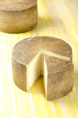 Whole wheel of sheep milk cheese over yellow wood.