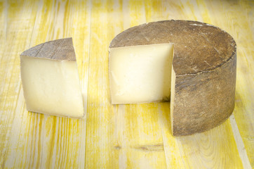 Whole wheel of sheep milk cheese over yellow wood.