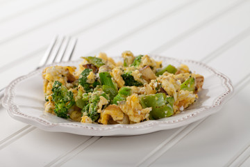 Scrambled eggs with broccoli, onions, and green bell peppers side view on white wood