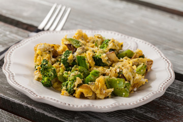 Scrambled eggs with broccoli, onions, and green bell peppers side view on a weathered old barn wood table