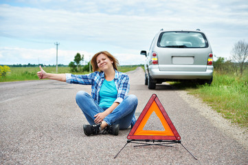 Woman sitting on road near emergency sign showing thumbs up