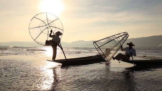 Burmese fisherman on bamboo boat catching fish in traditional way with handmade net. Inle lake, Myanmar, Burma