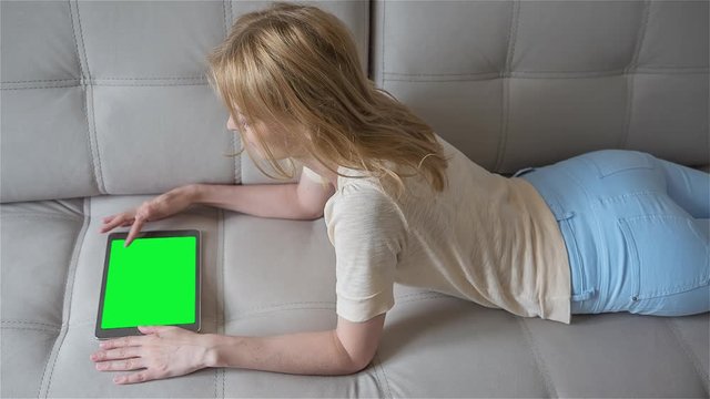High quality 10bit footage of Beautiful girl using tablet pc with pre-keyed green screen lying on sofa at home. Made from RAW footage.