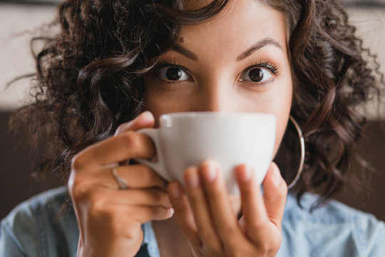 Eastern brunette curly girl drinking and smelling a cup of tea o