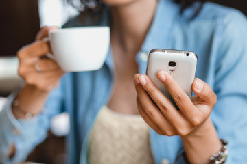 the hand of a woman with a phone and a mug of tea in the cafe