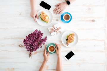 Hands of couple drinking coffee and eating croissants on table