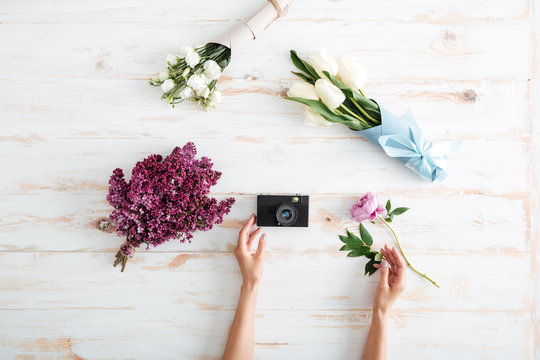 Hands of woman put flowers and photo camera on table