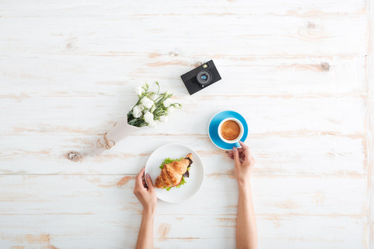 Hands of woman drinking coffee with croissant on wooden table