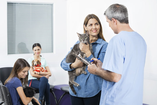 Woman Holding Cat While Looking At Nurse In Clinic
