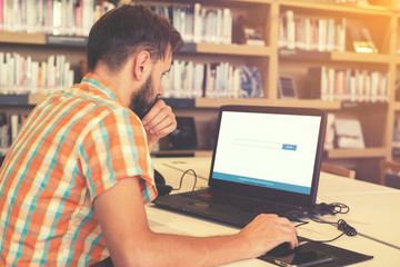 Side view shot of young business man hands busy working on his laptop sitting at  table in a library with vintage filter effect