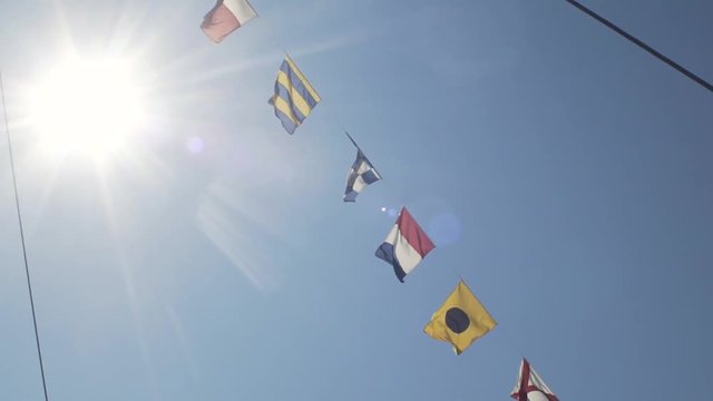 Slow motion shot of the nautical flags fluttering in the wind against blue sky with sun