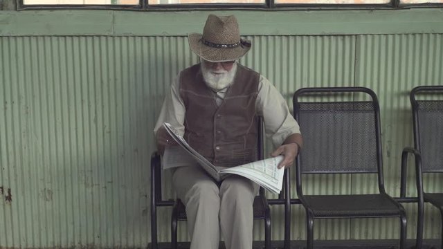 Senior man in eyeglasses with newspaper sitting on chair