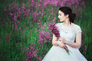 beautiful bride in a flower field. The girl in a white dress with a bouquet in a summer field at sunset