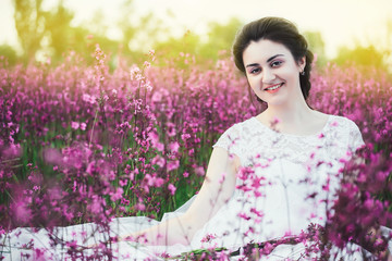 beautiful bride in a flower field. The girl in a white dress with a bouquet in a summer field at sunset