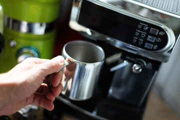 Hand führt eine Tasse zur Kaffeemaschine