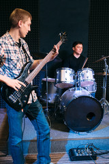 Bass guitar player and drummer play music . Front view on two musicians, making music with bass...