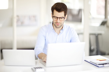 Solve the problem. Young businessman working on solving the problem on laptop at office.