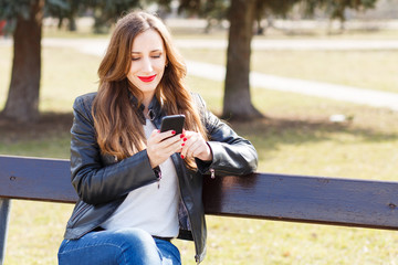 Fototapeta na wymiar Young smiling woman using smartphone in park