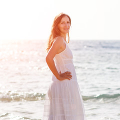 Fototapeta na wymiar Young woman in white dress standing at the sea