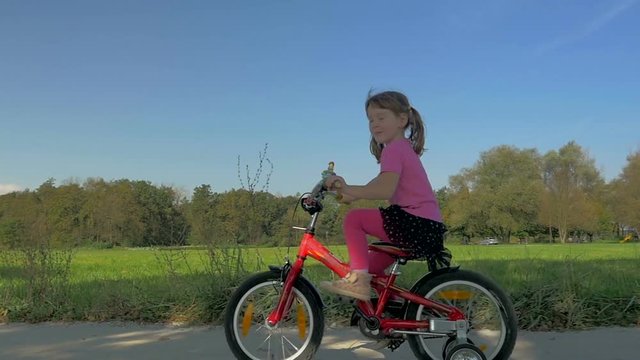 Dolly, low angle shot of cheerful, naughty little girl on her bike and shows tongue while cycling
