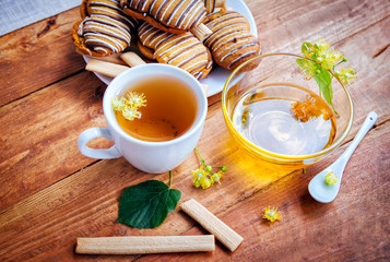 linden-blossom tea in a white cup honey in a glass bowl and pastry on a plate and on wooden background