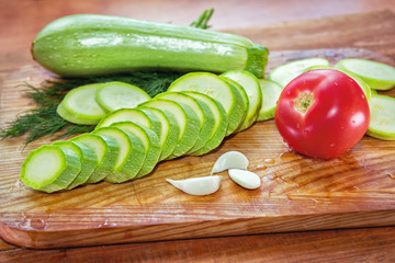 Sliced zucchini, ripe red tomato, garlic cloves and dill on a wooden cutting board on the table
