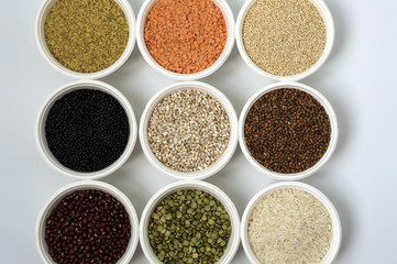 Different kinds of groats in small white bowls on white background