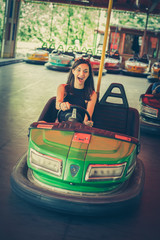 Cute young woman having fun in electric bumper car in amusement park