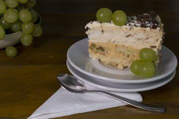Grapes and piece of cake on small white plate on wooden background - low key photo