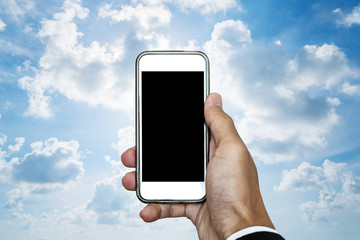 Hand holding mobile phone with blank space on screen, on blue sky with white clouds