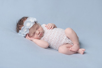 infant girl in a white dress sleeping on a blue background