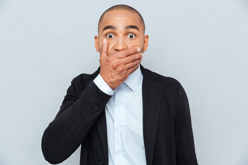 Handsome african man covering mouth with hand isolated on gray