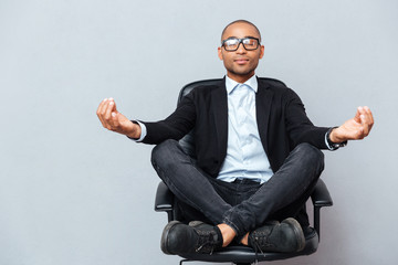 Attractive young man in glasses meditating on office chair