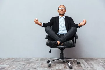 Fototapeten Entspannter afrikanischer junger Mann, der auf Bürostuhl sitzt und meditiert © Drobot Dean
