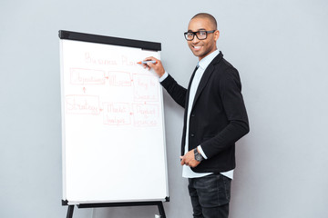 Smiling african man in glasses writing business plan on flipchart