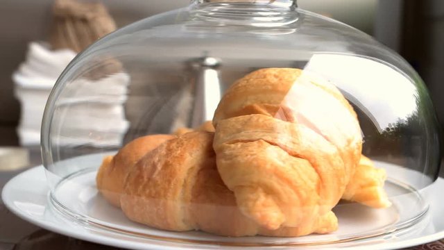 Fresh croissants in the white plate on the old wooden table under glass cover
