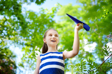 Fototapeta na wymiar Adorable little girl playing with blue paper plane outdoors