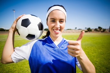 Happy soccer player holding a ball and showing her thumbs up