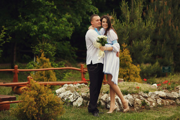 Fototapeta premium Groom in an embroidered blue shirt hugs a tender brunette bride