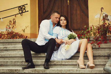 Obraz premium Groom hugs a bride in a short dress sitting on the stairs