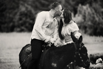 Groom kisses a bride reaching to him while he sits on a donkey