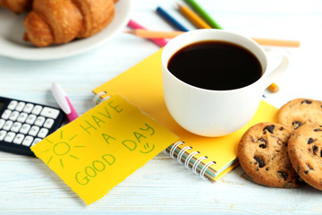 Piece of note paper with cup of coffee and cookies on blue woode
