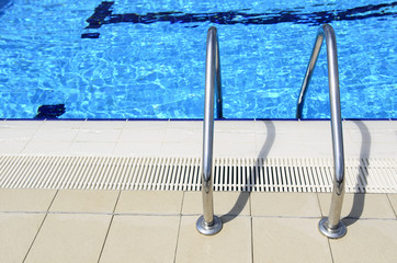 Detail from open olympic swimming pool with stairs and clear blue water at summer