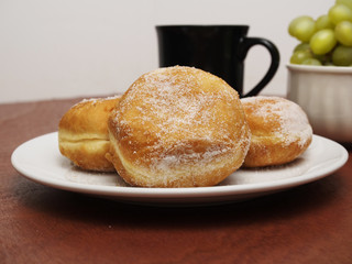 Donuts on a plate with a tea cup and plate with grapes in background.