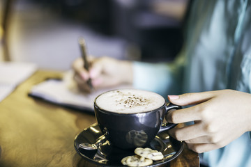 Fototapeta na wymiar woman in holding a cup of cappuccino while writing 