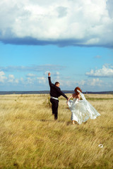 Bride and groom walk jumping along the field in a shiny weather