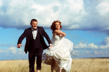 Bride rises her dress up walking across the field with a groom u