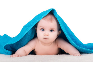 cute baby child with big eyes under blue towel on white, isolated. baby lying on a soft blanket, looking at the camera and tries to crawl on his belly